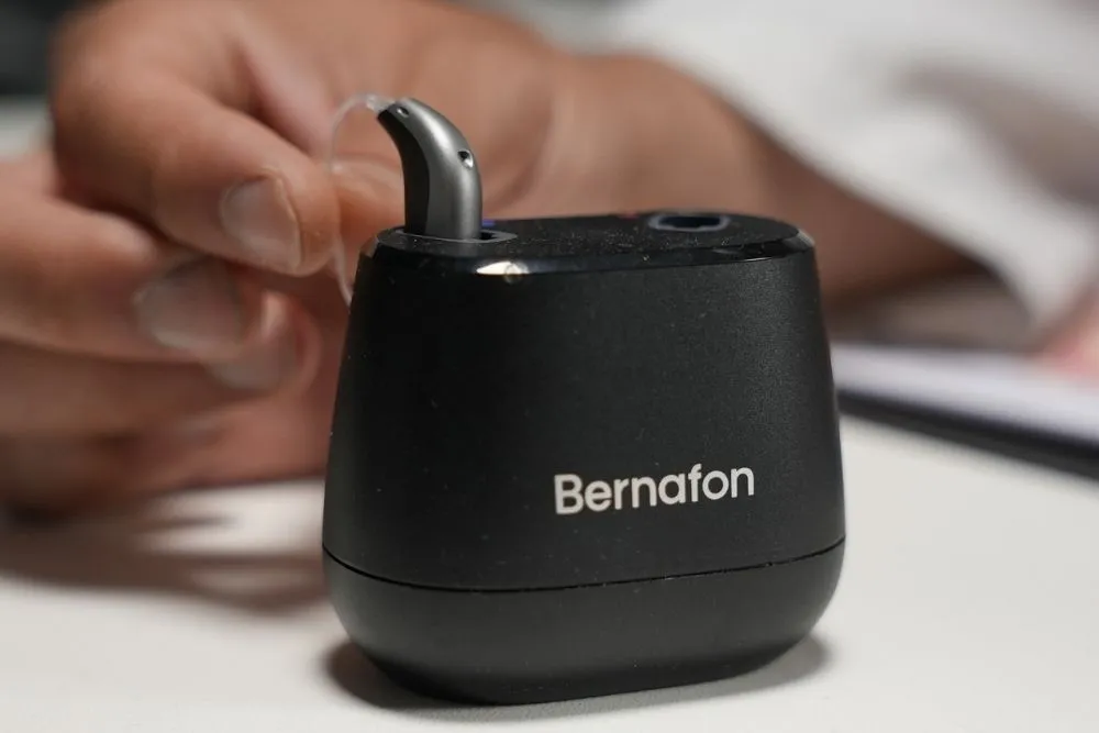 Audífono recargable Bernafon sostenido junto a su cargador negro