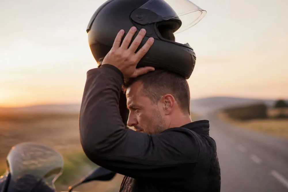 Motorista quitándose el casco en una carretera al atardecer
